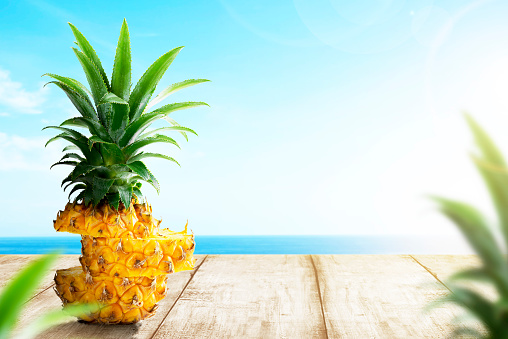 Slice of fresh pineapple on wooden table with ocean view and blue sky background