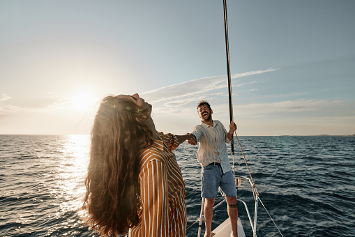 Cheerful couple having fun while holding hands and dancing on a boat in summer day. Copy space.