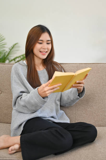 istock Portrait, Beautiful Asian female sits on her sofa, reading a book 1426138652