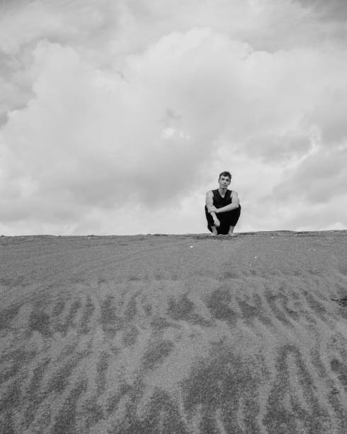 istock Lone man sitting barefoot on the sand in sandy desert 1426145122
