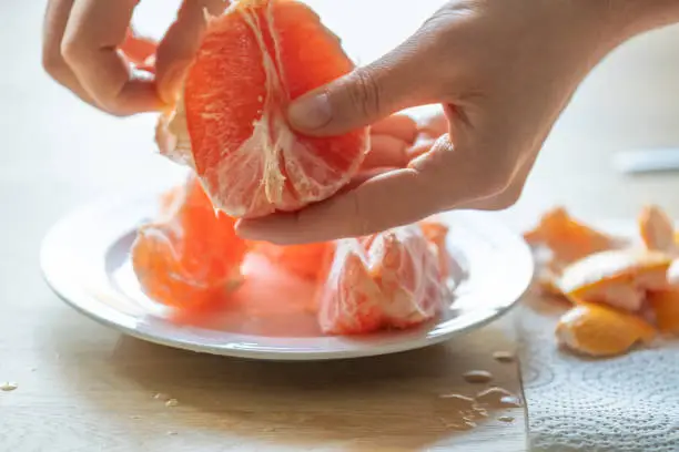 grapefruit.Citrus fruit.Womans hands peeling a grapefruit.Fresh and juicy grapefruit.Splashes and drops of grapefruit juice.Fruit for breakfast. breakfast preparation