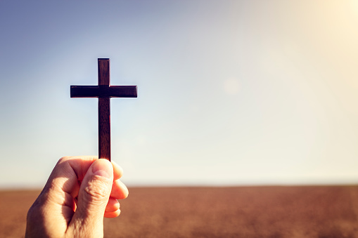 Holding up religious cross crucifix to sky and earth field background