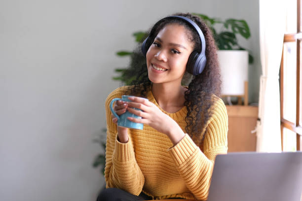 istock Smiling young asian woman using laptop web camera while holding a cup of coffee and wearing headphones in the living room at home. 1426160692