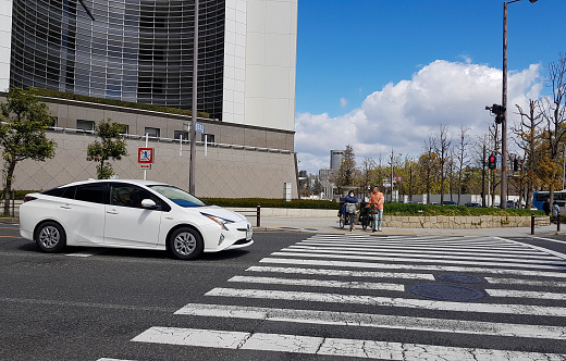 Osaka, Japan - April 10, 2019: Situation at a pedestrian crossing, where a white sporty car stops when a couple riding a bicycle crosses at the crossing.