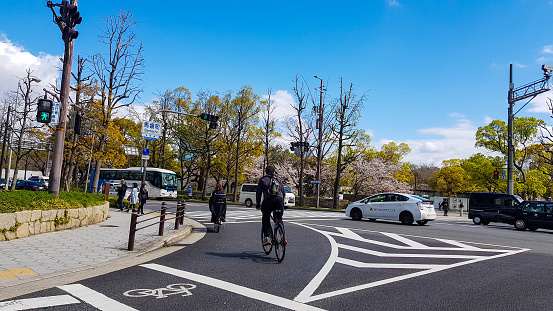 Osaka, Japan - April 10, 2019: Situation at a pedestrian crossing, where a white sporty car stops when a couple riding a bicycle crosses at the crossing.