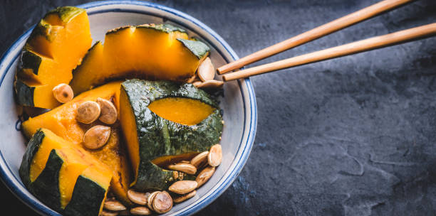 istock Delicious  Kabocha Squash (Japanese Pumpkin) recipe. Japanese Simmered Kabocha cooked in savory dashi broth seasoned with soy sauce and sake with pumpkin seeds, close up, dark background. Web banner 1426177607