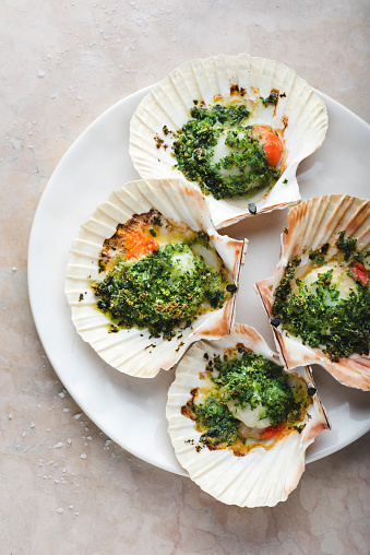 Recipe Baked sea scallops. Recipe with chopped parsley and dry grated bread on the white plate on the soft rose marble background, close-up, medium tone. Mediterranean seafood recipes