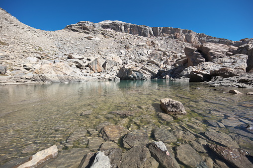 Small mountain lake located 200m east of the Col de Serenne 2674m with on its banks large blocks of Guillestre red marble from the cliff of La Mortice Sud 3169m