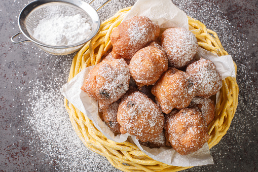 Sweet donuts oliebollen with raisins and powdered sugar close-up in a basket on the table. Horizontal top view from above