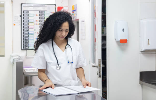 enfermeira focada na estação de enfermeiras olhando para um caderno - nurse reaching women doctor - fotografias e filmes do acervo