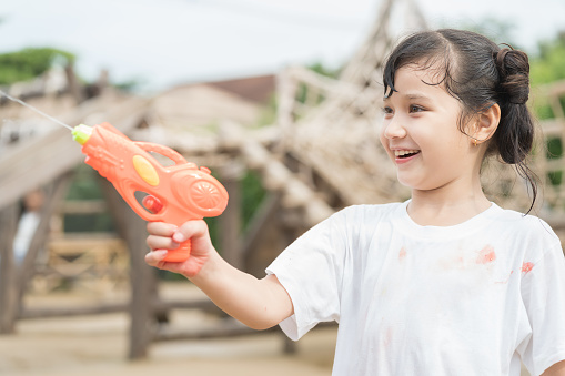 Child girl has fun playing with water gun on hot summer day outdoors. Kid girl having fun with water outdoors