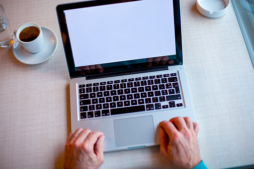 Top view of senior man's hands on open laptop. A blank screen for your image.