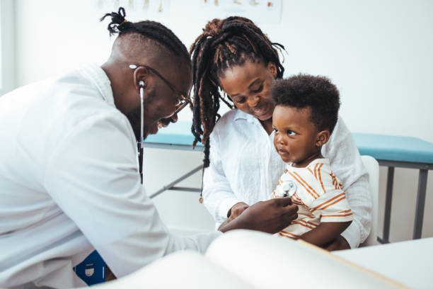 A happy toddler boy sits in his mother' lap at the pediatrician stock photo