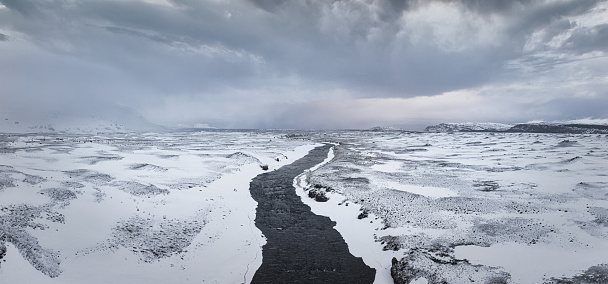Frozen, snow covered landscape close to the famous Hekla Volcano with river floating through the Highlands of Iceland under snow cloudscape in winter. Aerial Drone Point of View Stitched Panorama. Iceland Highlands, South Central Iceland, Nordic Countries, Northern Europe.
