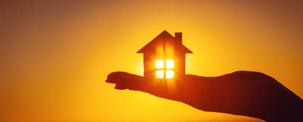 istock Woman's hand holding a model of a house on sunset evening 1426201498