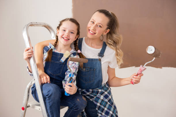 A beautiful blonde woman, together with cute 8-year-old child, started the renovation. The girl is sitting on the ladder, and mother is hugging her. The two of them are dressed in denim style A beautiful blonde woman, together with cute 8-year-old child, started the renovation. The girl is sitting on the ladder, and mother is hugging her. The two of them are dressed in denim style. mum new boyfriend stock pictures, royalty-free photos & images