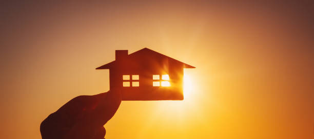 istock Woman's hand holding a model of a house on sunset evening 1426206557
