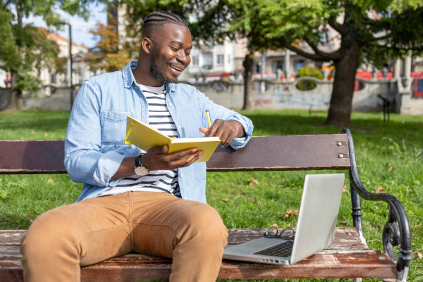 istock Cheerful adult student sitting in a park and using laptop when holding a book 1426206684