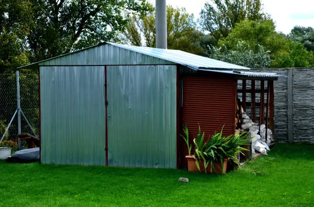 Sheet metal garage used as a garden house. A grassy yard with a metal construction of galvanized sheets. store lawnmower, bikes and gardening tools