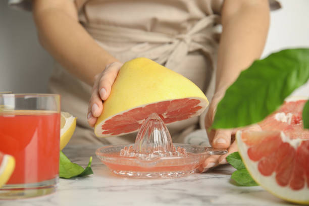 istock Woman squeezing pink pomelo juice at white marble table, closeup 1426209896