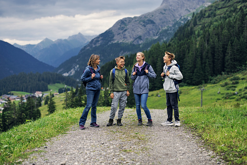 Family is hiking in the Alps - Vorarlberg, Austria. They are walking on the path among green meadows high in the mountains.\nCanon R5