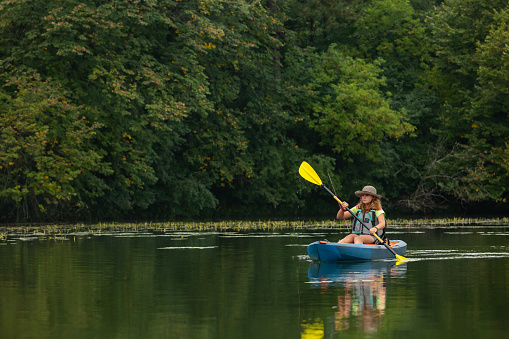 Girl in her kayak with a fishing pole behind her. She is paddling to find the perfect spot to cast her line.