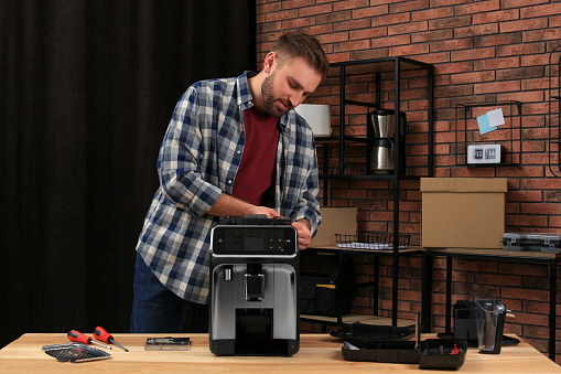 Man fixing coffee machine at table indoors