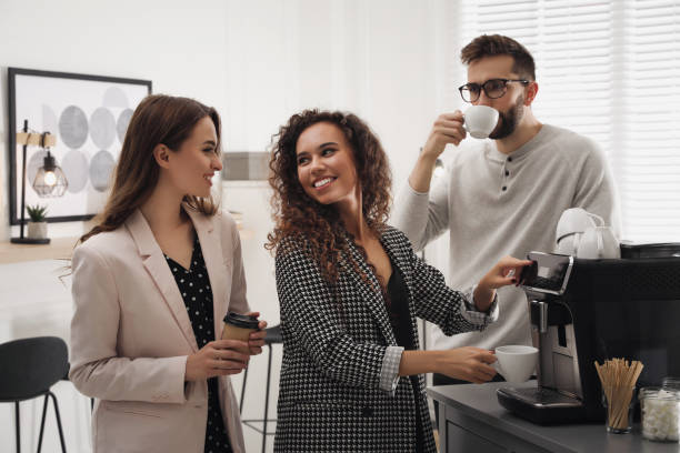 donna afroamericana che parla con i colleghi mentre usa la moderna macchina da caffè in ufficio - espresso coffee cafe making foto e immagini stock