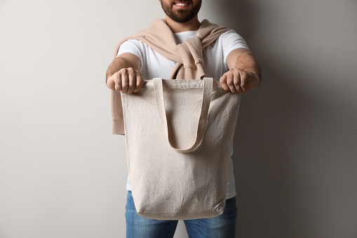 Happy young man with eco bag on light background, closeup