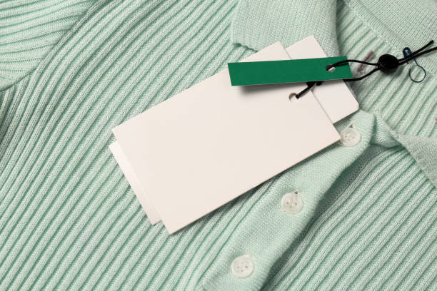 Blank white tags on mint knitted shirt, top view. Space for text