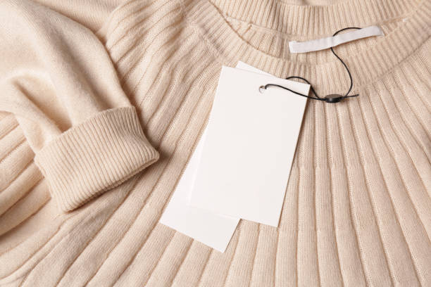 Blank white tags on beige sweater, top view. Space for text