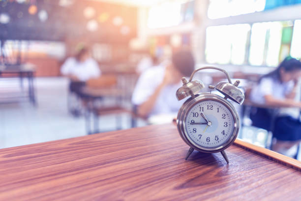 teste exame em conceito de educação,despertador na mesa de madeira, exames de alunos em sala de aula , testes de bolsas de estudo para estudo no exterior - old fashioned desk student book - fotografias e filmes do acervo