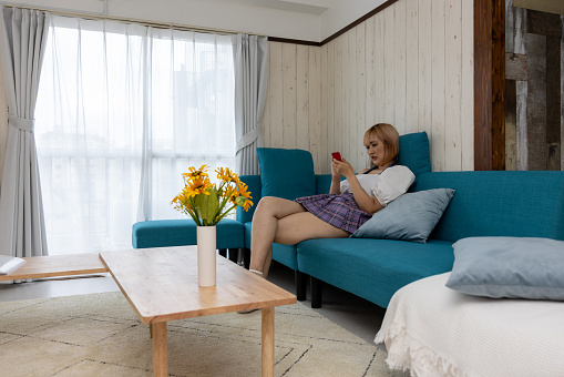 Young woman sitting on sofa and reading message on smart phone