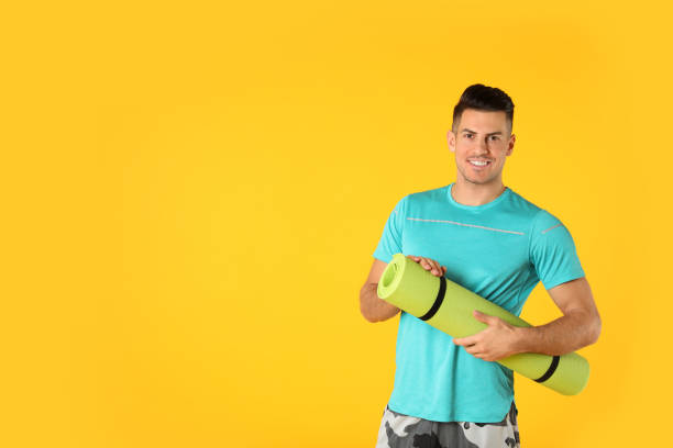istock Handsome man with yoga mat on yellow background. Space for text 1426218196