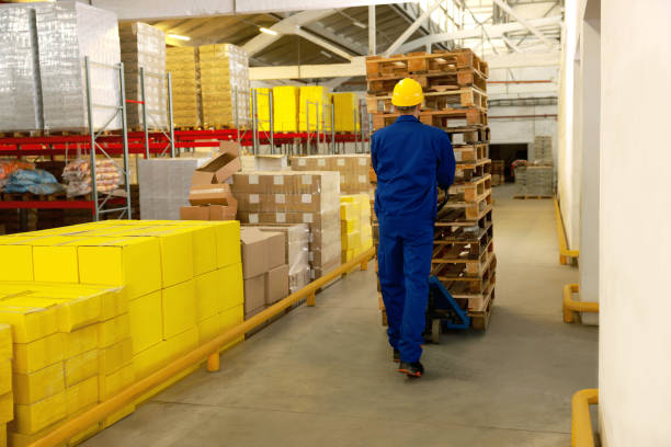 istock Worker moving wooden pallets with manual forklift in warehouse, back view 1426218537