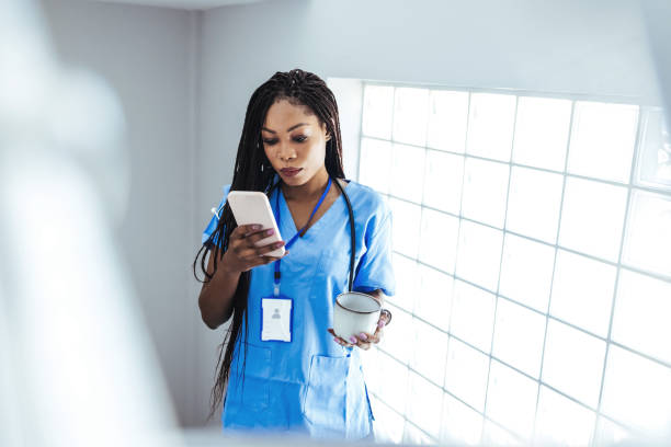 istock African female surgeon wearing scrubs reading text message on her mobile phone while standing in hospital. 1426223186
