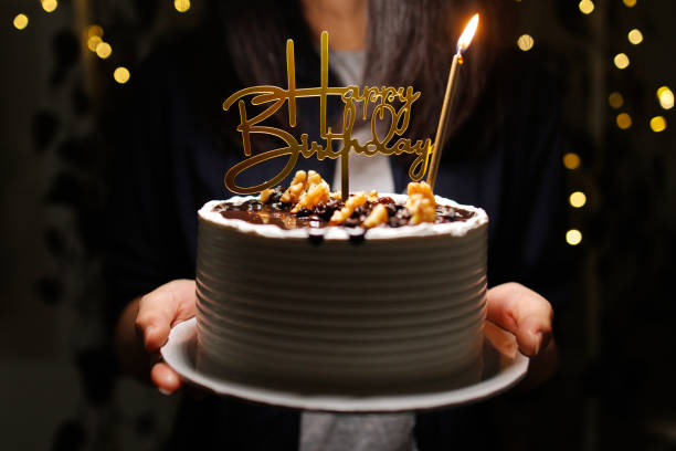 Woman holding birthday cake decorated with golden happy birthday sign and candle stock photo