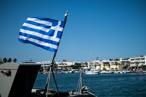 Sail boat mast with a waving Greek flag against a cloudless blue sky.