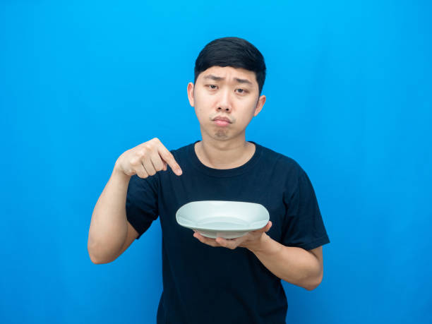 istock Man hungry point finger at dish in hand sad face blue background 1426229927