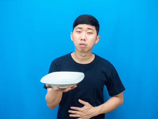 istock Man holding dish and touch belly feeling hungry blue background 1426229928