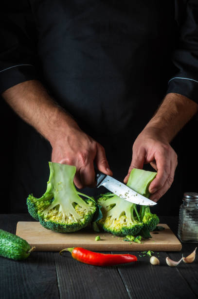 istock Cook cuts fresh Broccoli with a knife for salad on vintage kitchen table with fresh vegetables. Cooking and restaurant or cafe concept 1426229980
