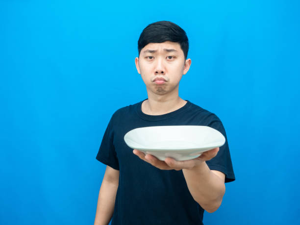 istock Hungry man holding empty dish gesture want food blue background 1426230280