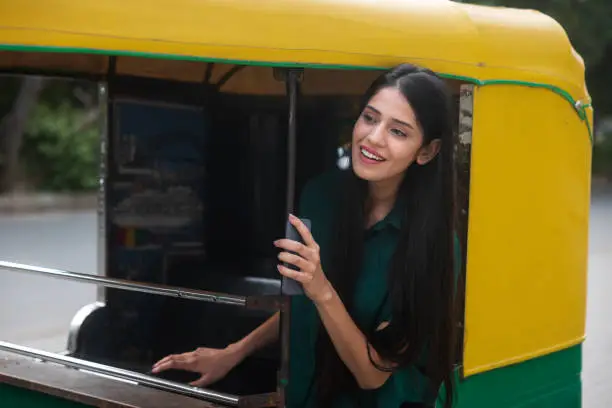 Indian woman using his phone, while getting off a rickshaw