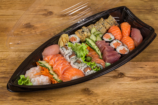 Set of sushi rolls in plastic box on wooden table. Sushi for take away or delivery of sushi in plastic container.
