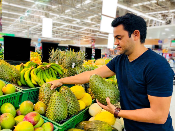 Man choosing soursop fruit in a market Latin man choosing fruits in a market annona muricata stock pictures, royalty-free photos & images
