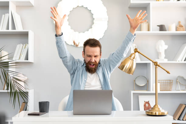Young successful man sitting at the table raising his hands