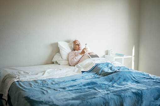 Senior woman sick in bed takes temperature