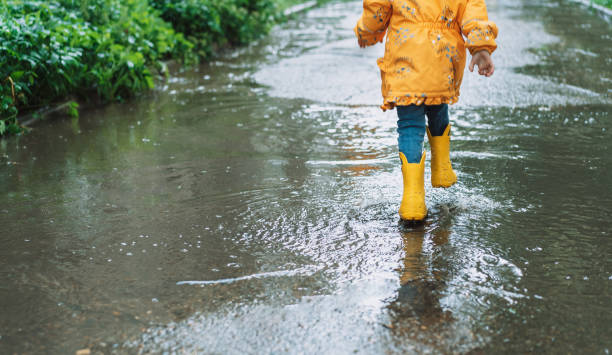 istock Girl in yellow jacket and rubber boots runs through the puddles 1426240017