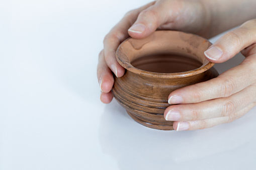 Hands of a potter on an ancient clay pot isolated on white with copy space. A close-up.