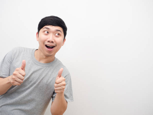 istock Man grey shirt smiling and thumb up looking at copy space white isolated 1426245238